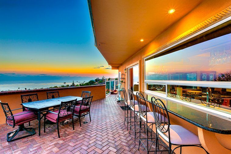 a balcony with a table and chairs overlooking the ocean at sunset