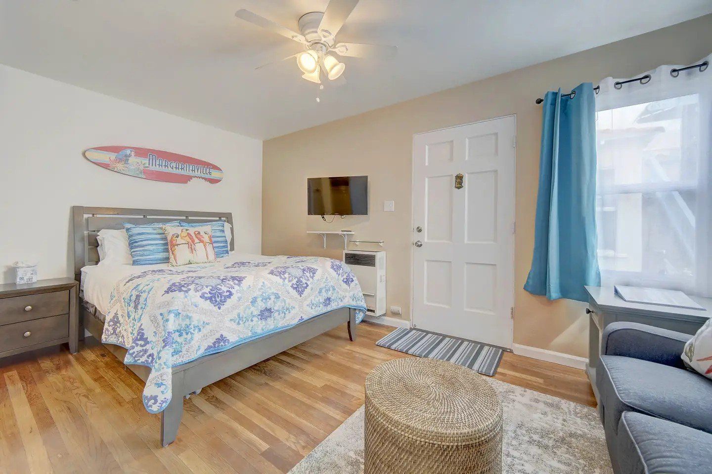 A bedroom with a king size bed , a couch , a television and a surfboard on the wall.