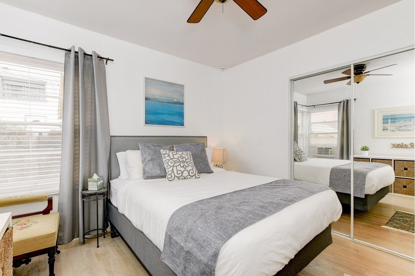 A bedroom with a bed , chair , mirror and ceiling fan.