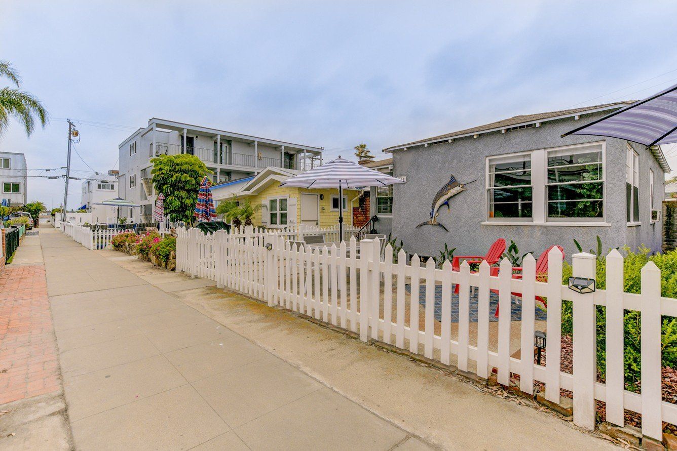 a white picket fence surrounds a house on the side of a street .