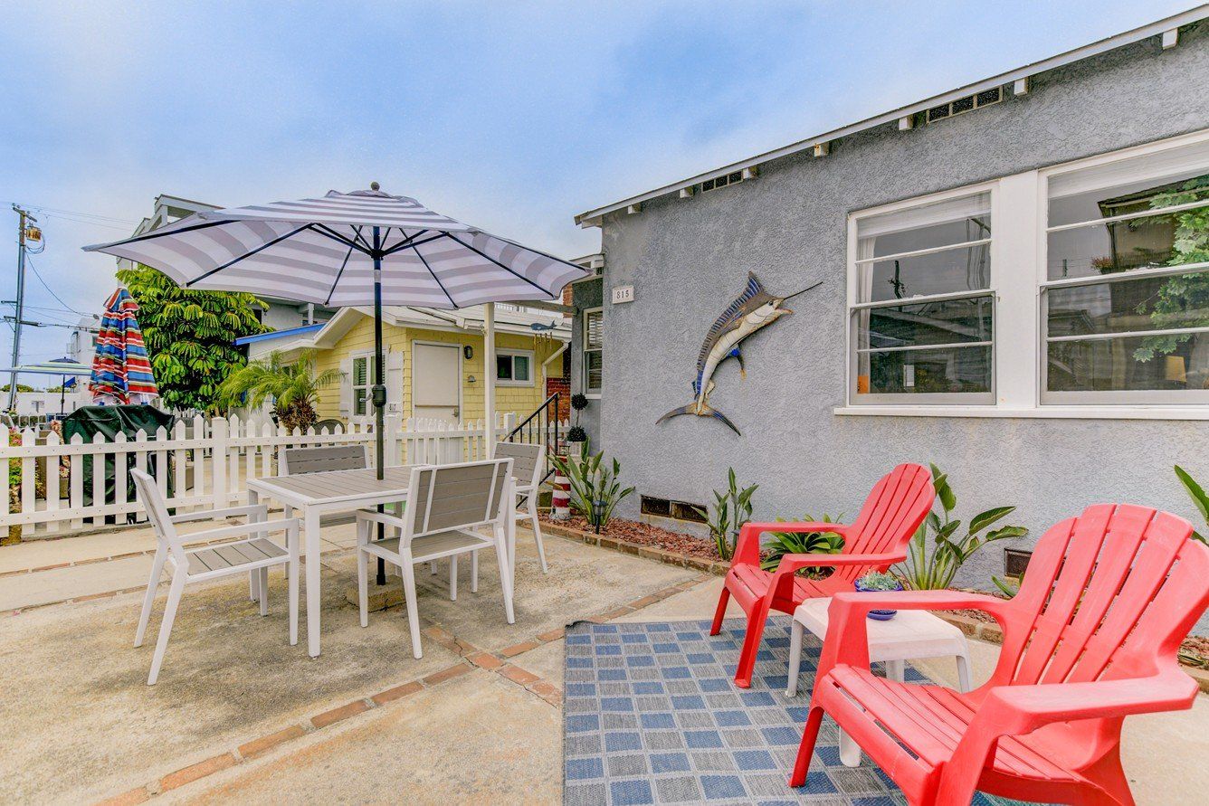 a patio with red chairs , a table and an umbrella in front of a house .