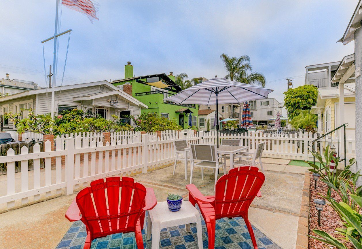 a patio with two red chairs , a table and an umbrella .