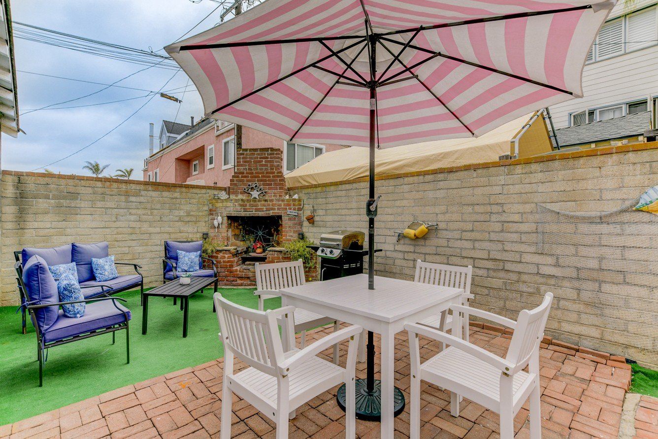 a pink and white striped umbrella is sitting on a patio next to a table and chairs .