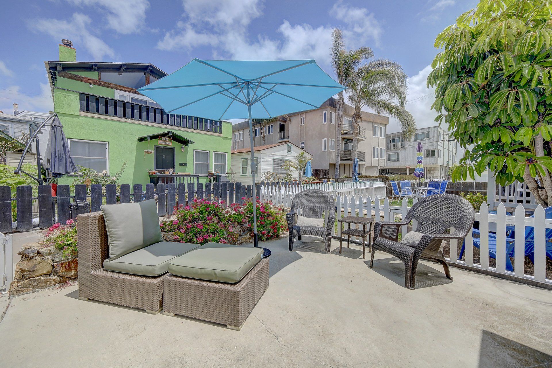 a patio with a blue umbrella and a green house in the background .