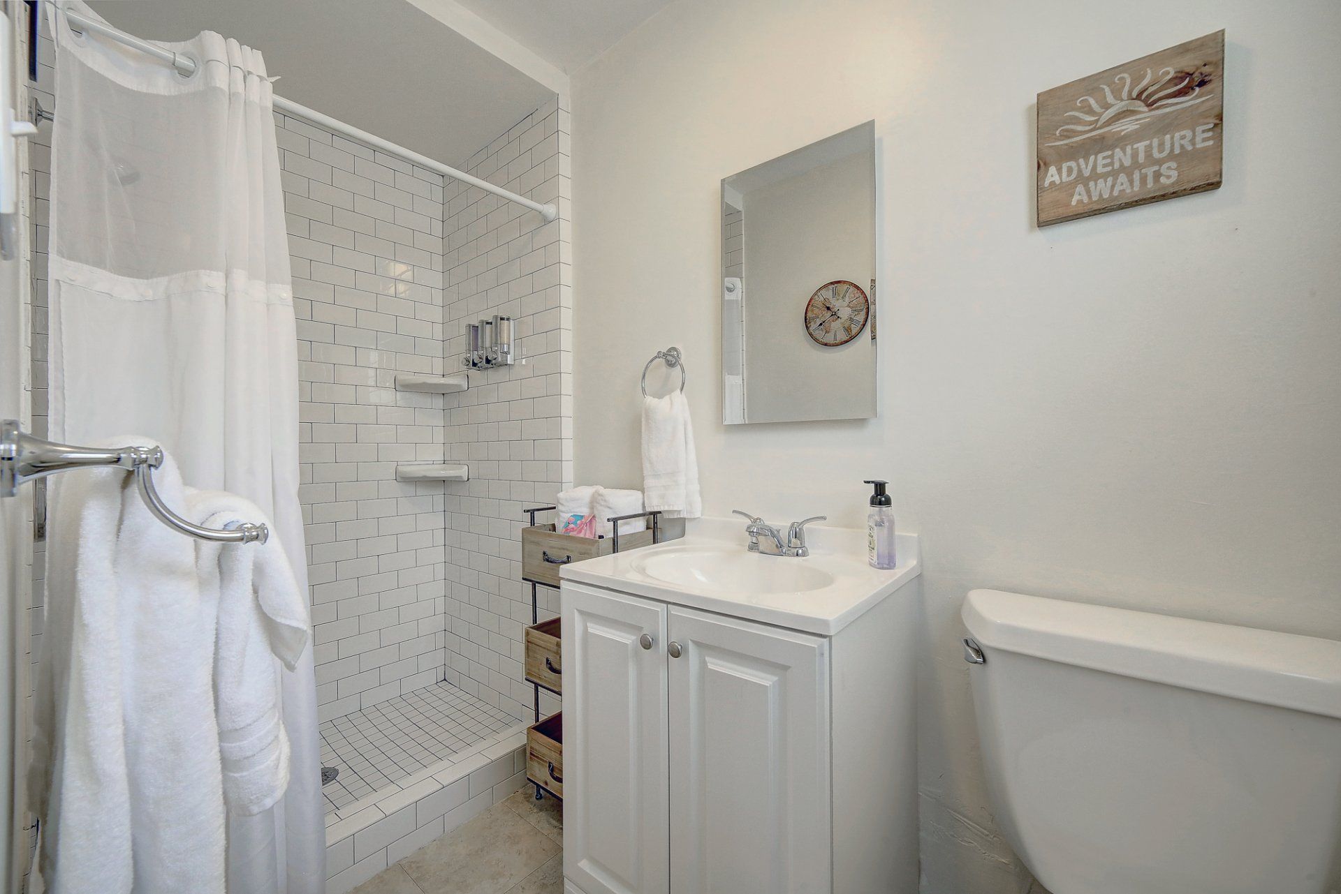 A bathroom with a shower , sink , toilet and mirror.