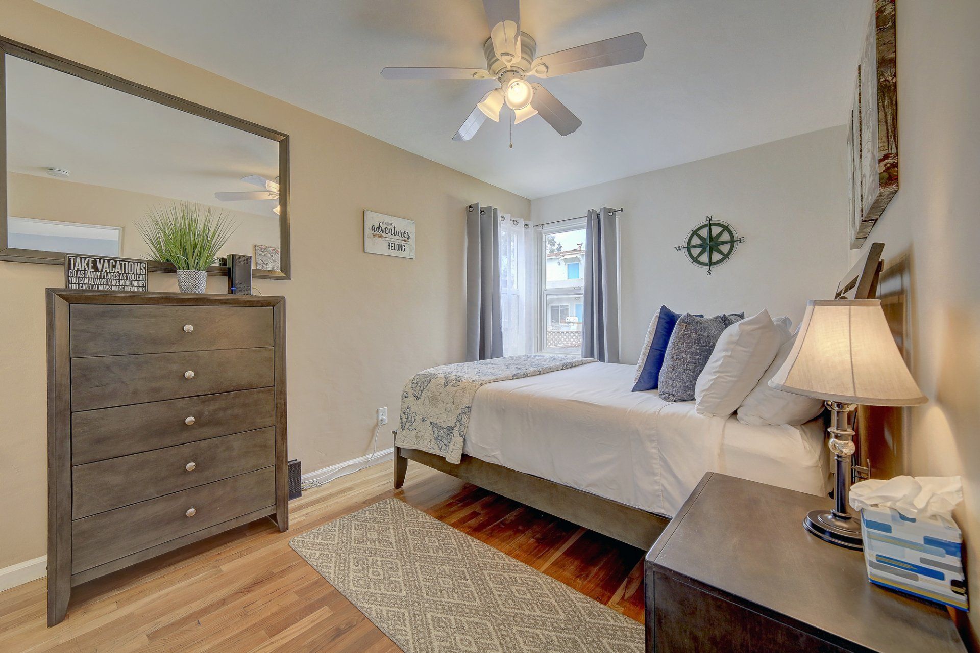 A bedroom with a bed , dresser , nightstand , mirror and ceiling fan.