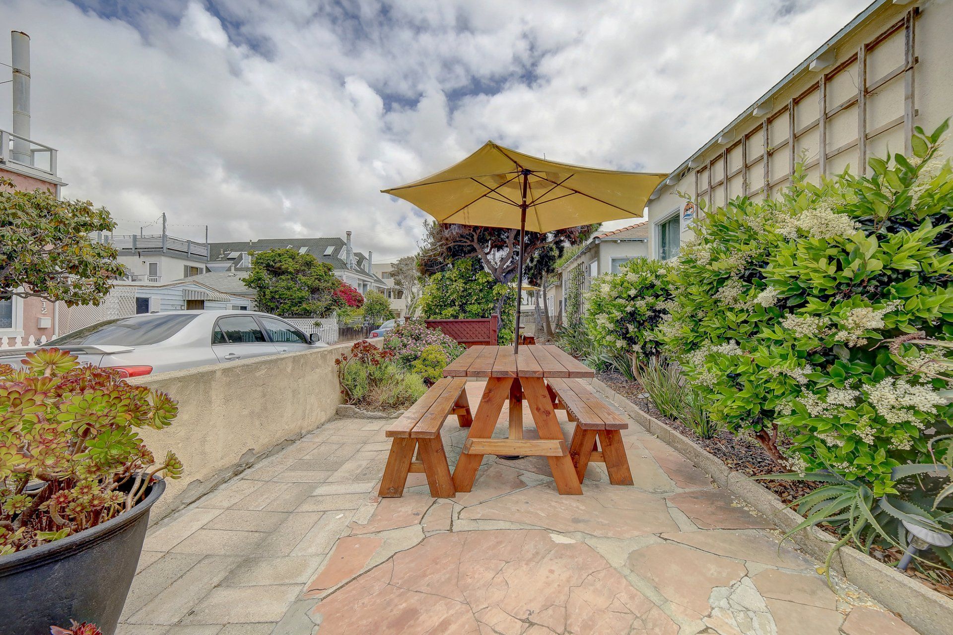 A wooden picnic table with a yellow umbrella on a patio.