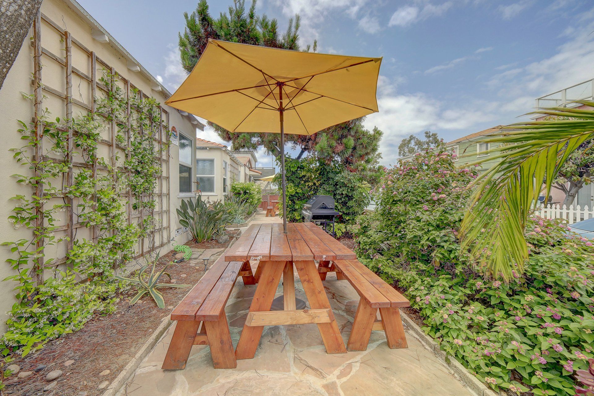 A wooden picnic table with a yellow umbrella in the backyard.