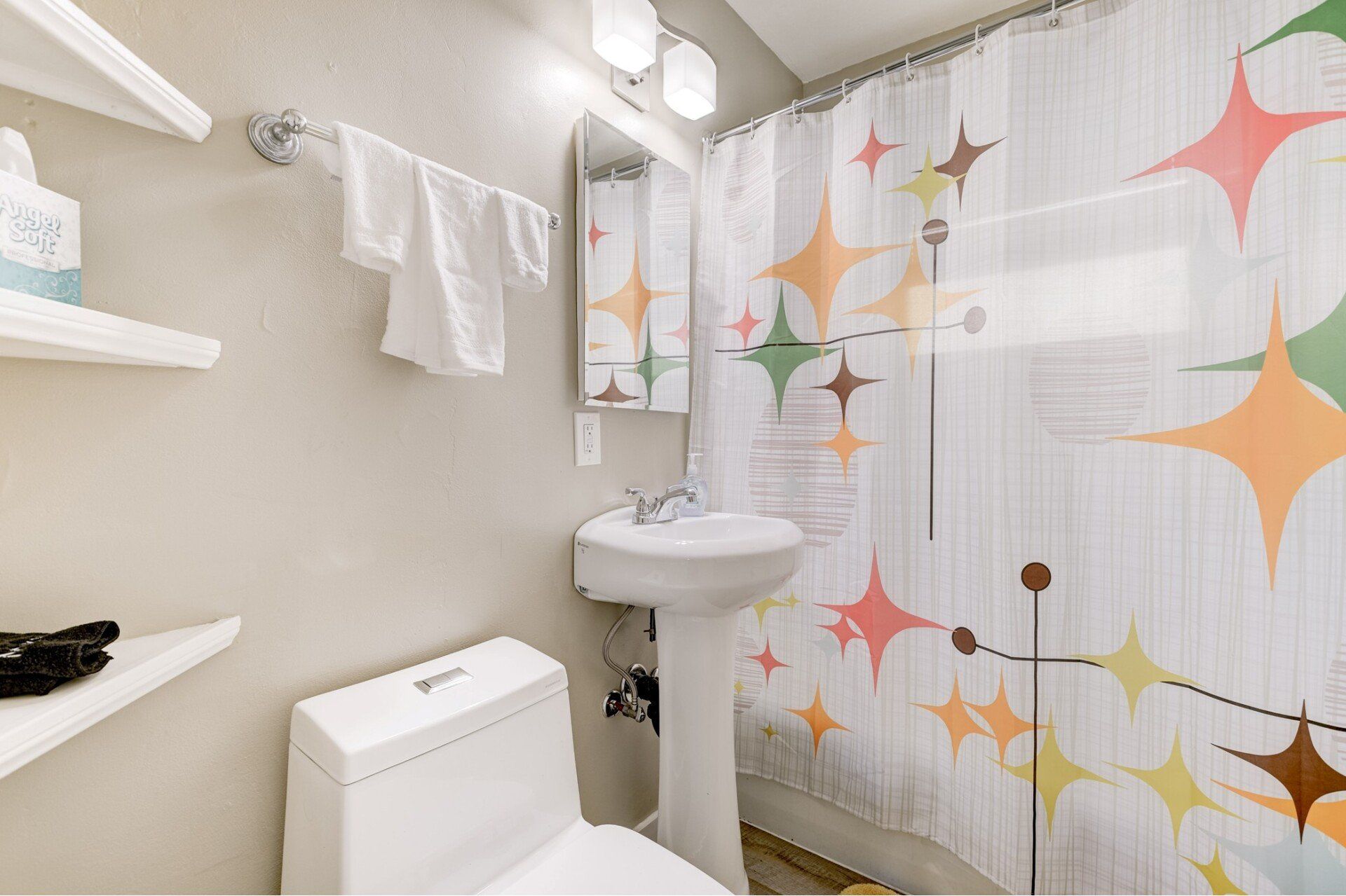 A bathroom with a toilet , sink , shower curtain and mirror.