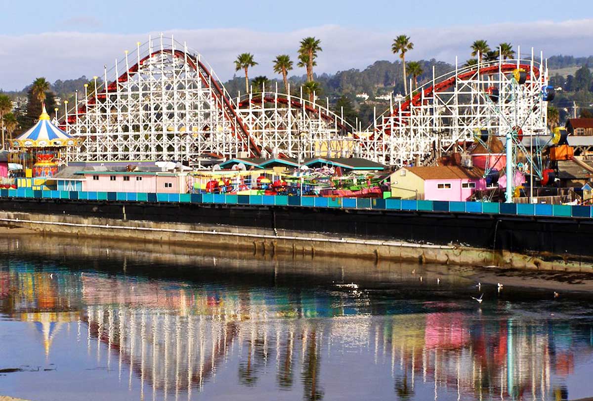 a roller coaster is reflected in the water at an amusement park .