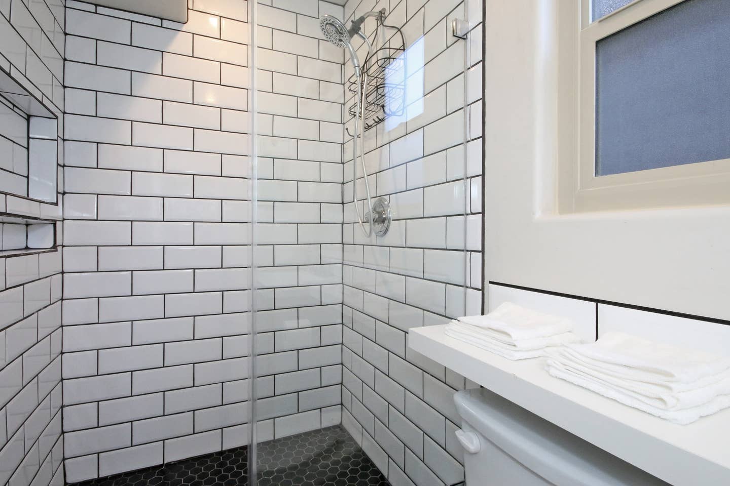 A bathroom with white tiles and a walk in shower