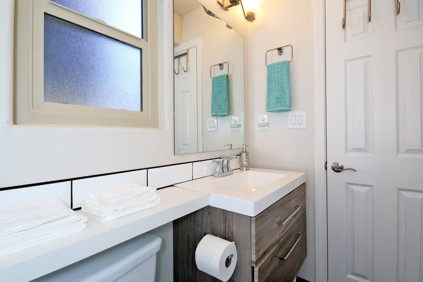 A bathroom with a sink , toilet , mirror and window.