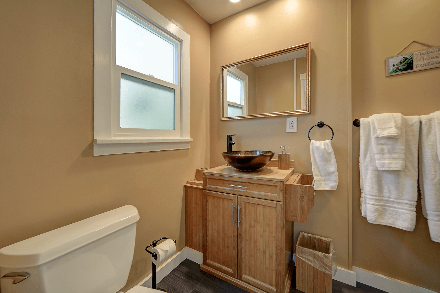 a bathroom with a toilet , sink , mirror and window .