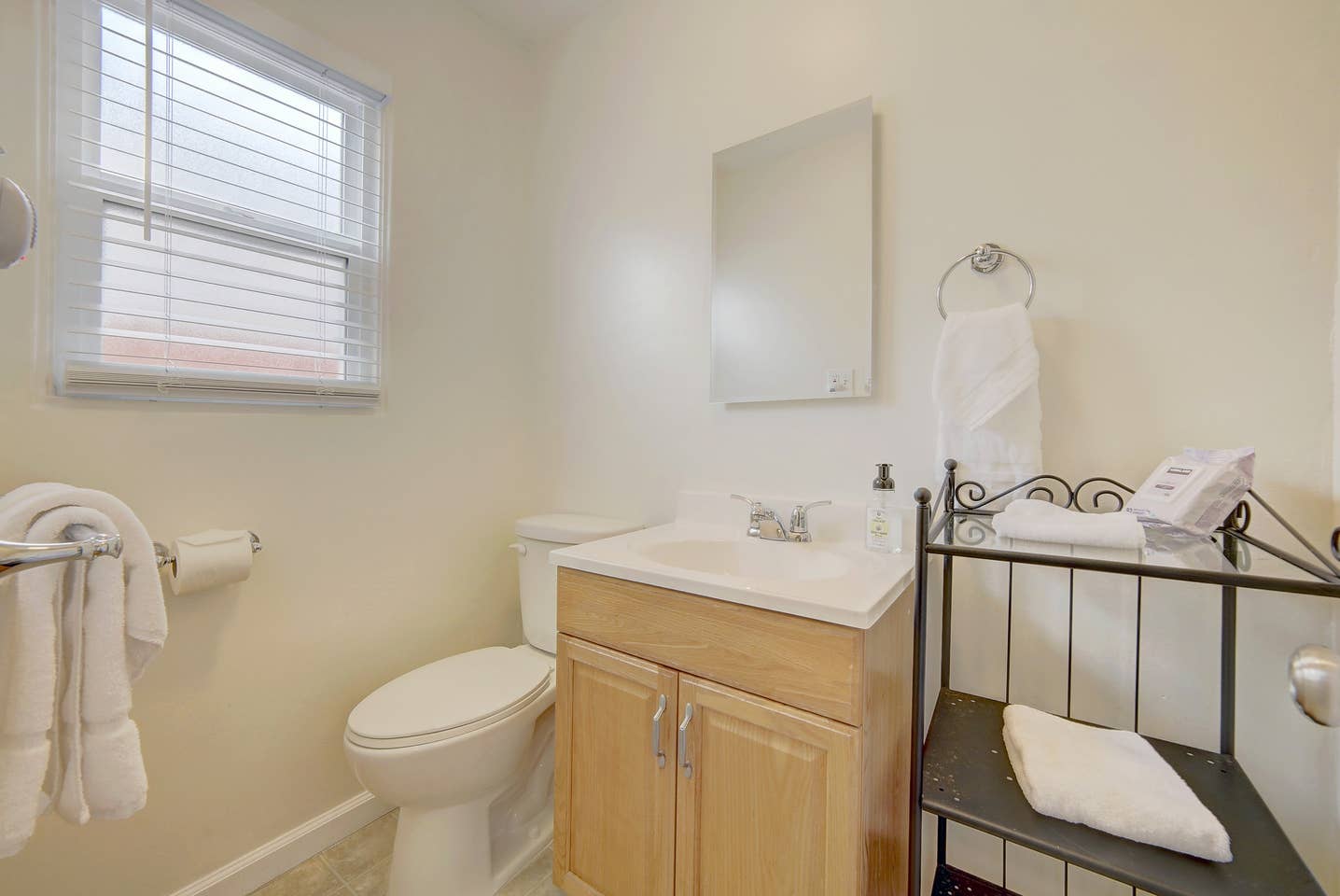 A bathroom with a toilet , sink , mirror and window.