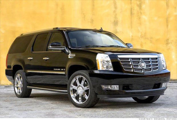 A black cadillac escalade is parked in front of a yellow wall