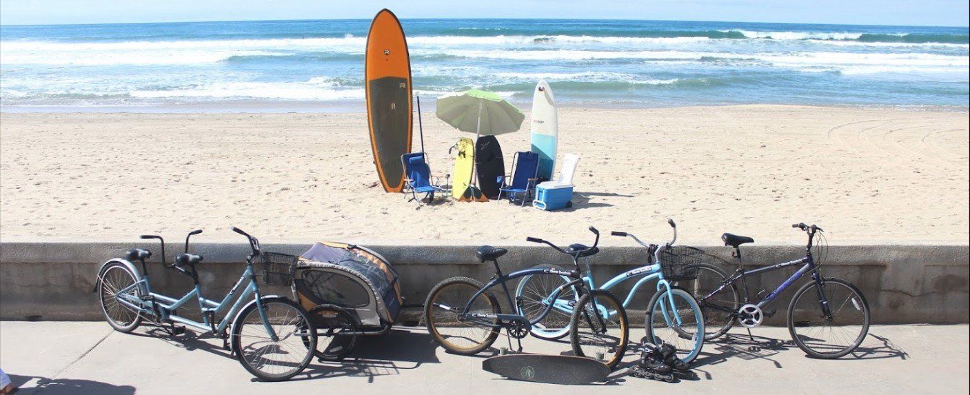 a row of bicycles are parked on the side of a beach next to a surfboard .