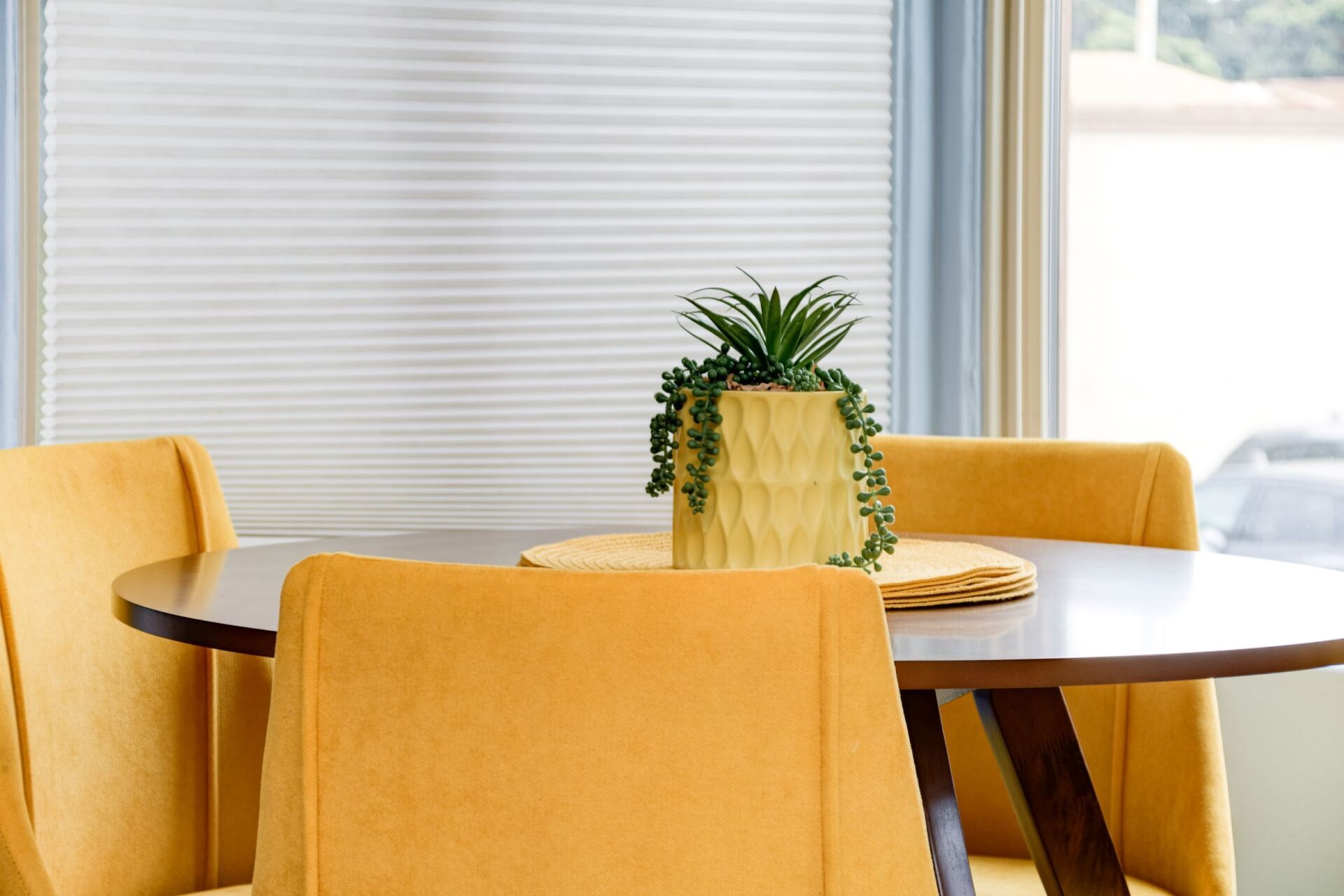 A dining room table with yellow chairs and a potted plant on it.