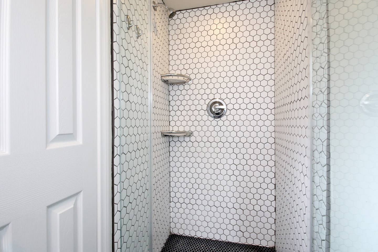 A shower with a glass door and white tiles on the wall.