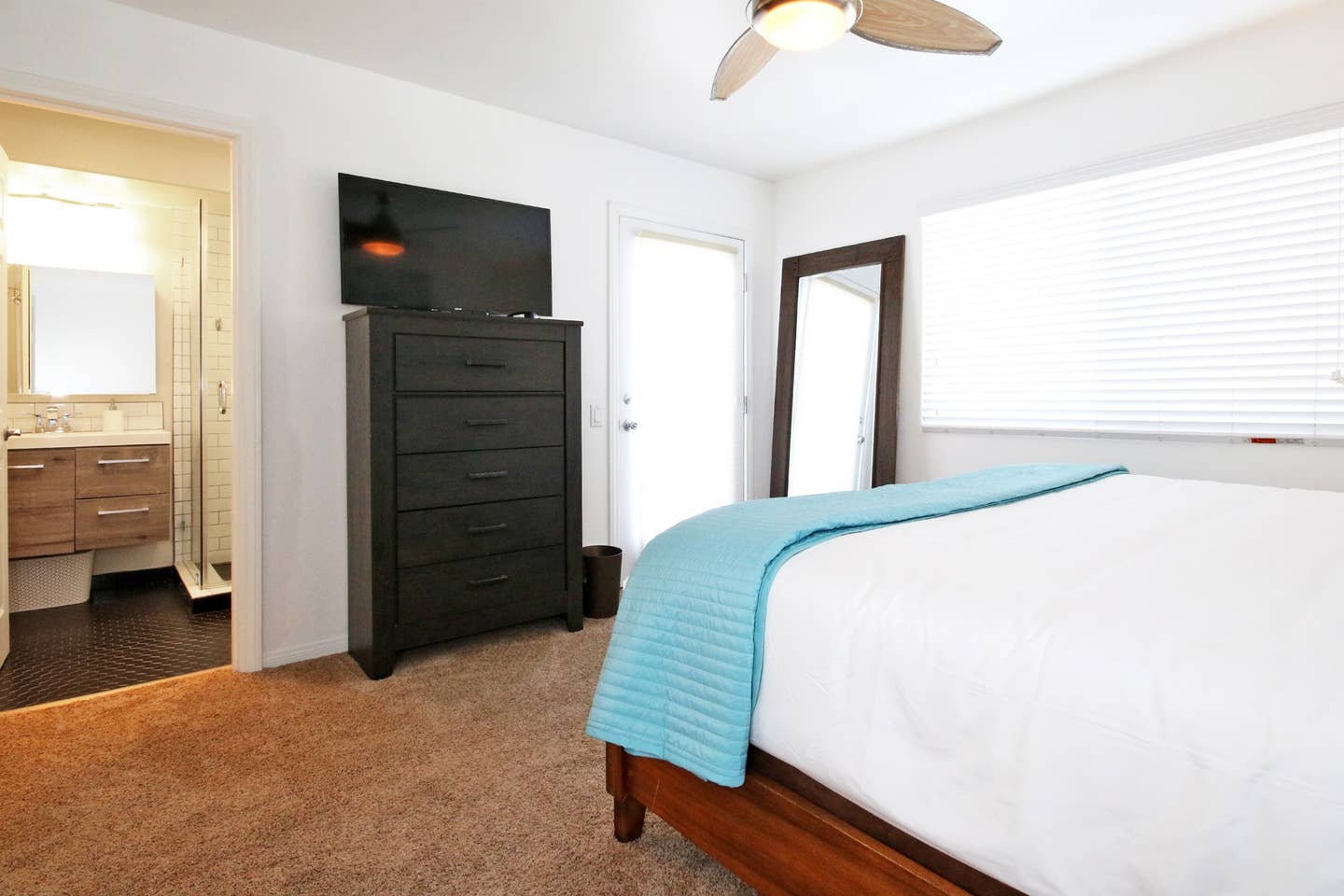 A bedroom with a bed , dresser , television and ceiling fan.