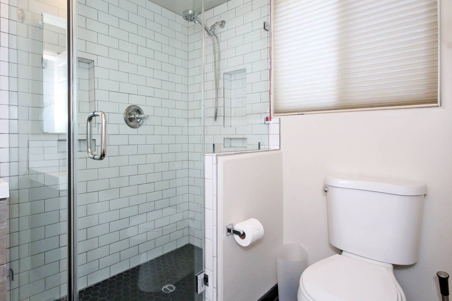 A bathroom with a toilet , shower , and window.