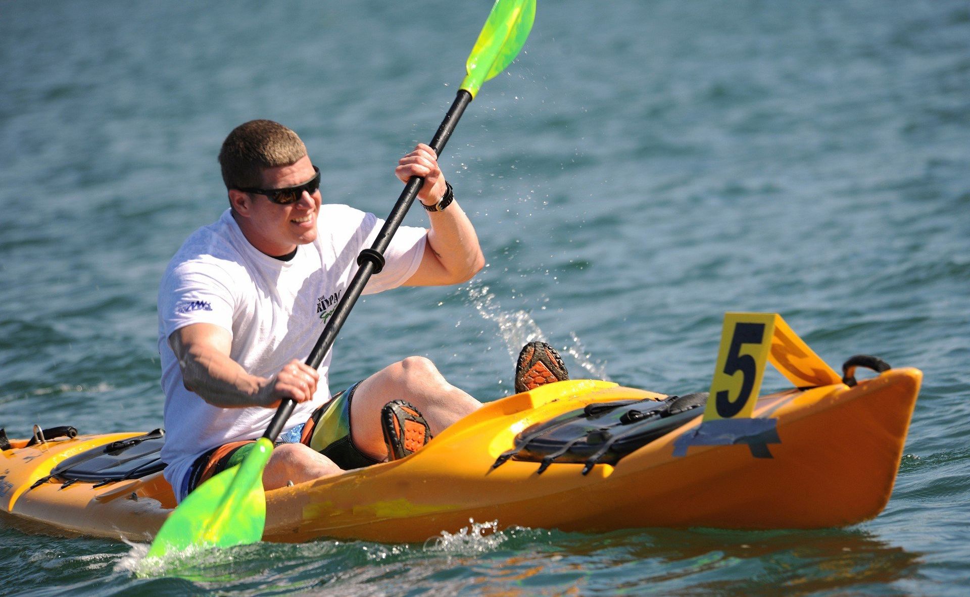 a man is paddling a yellow kayak with the number 5 on the side .