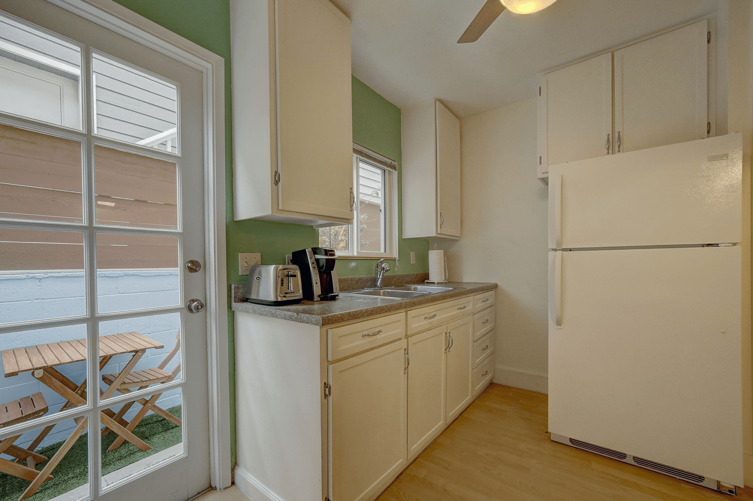 A kitchen with white cabinets , a refrigerator , a toaster , and a sliding glass door.