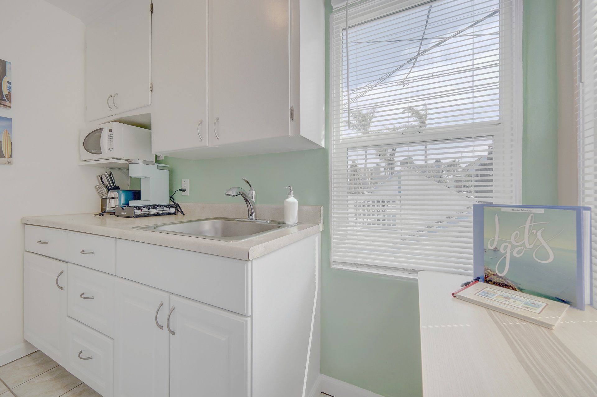 A kitchen with white cabinets , a sink , a microwave , and a window.