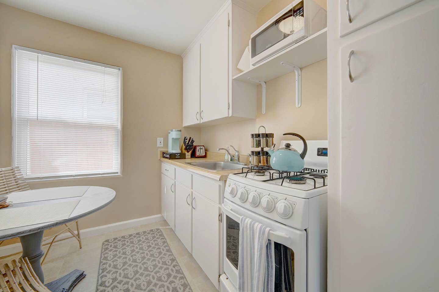 a kitchen with white cabinets , a stove , a microwave , and a table .