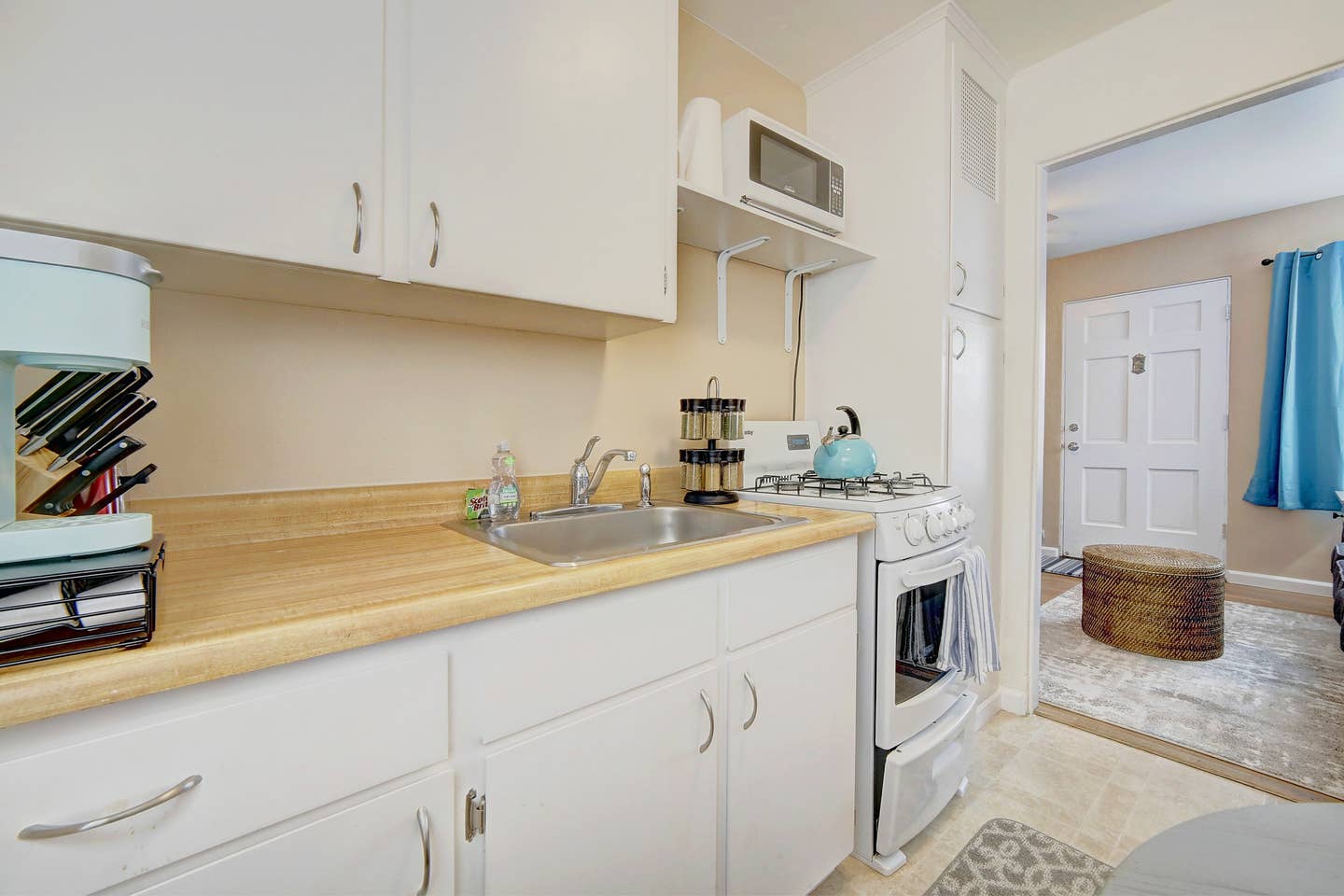 a kitchen with white cabinets , a sink , stove and microwave .