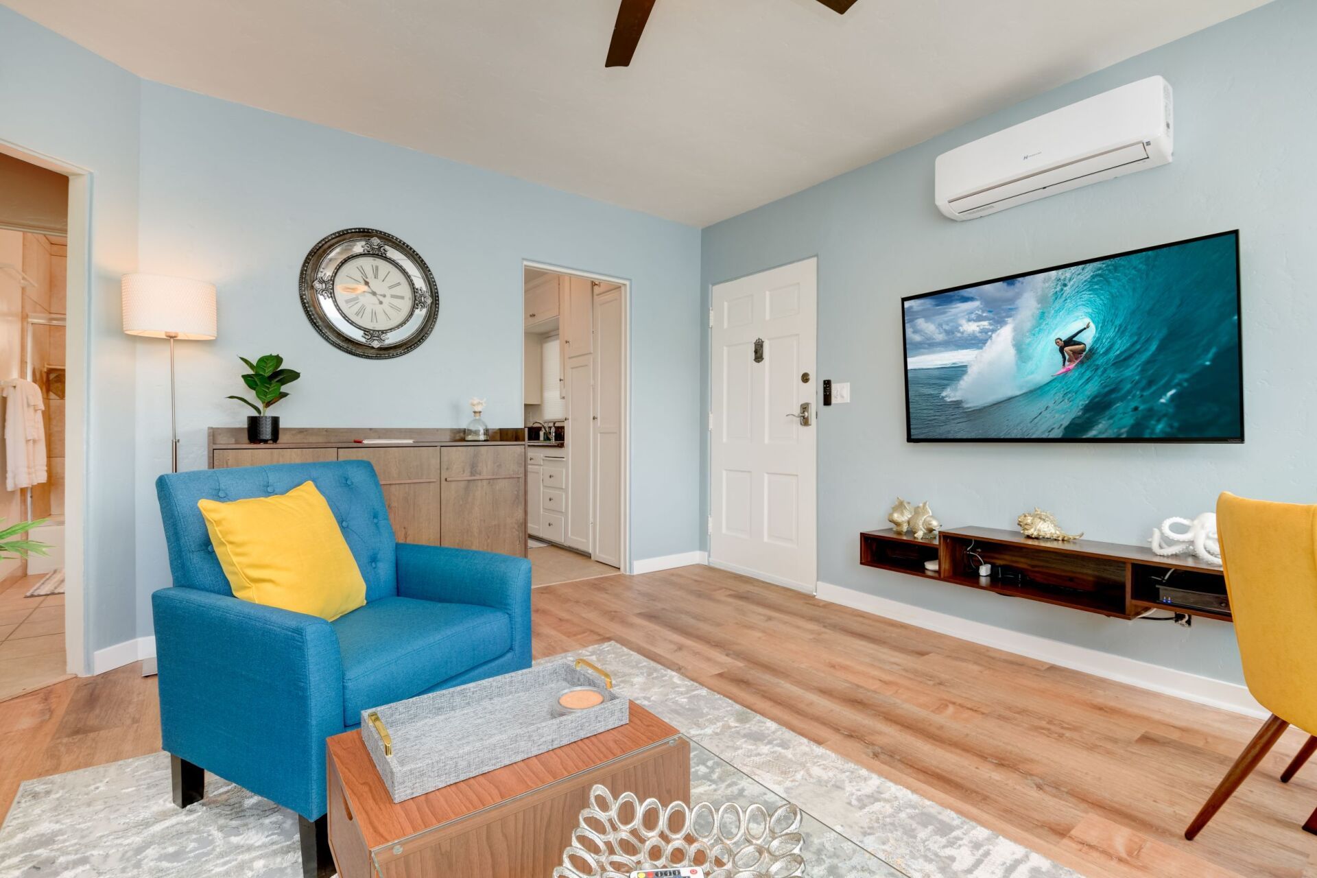 A living room with a blue chair , yellow chair and a flat screen tv.