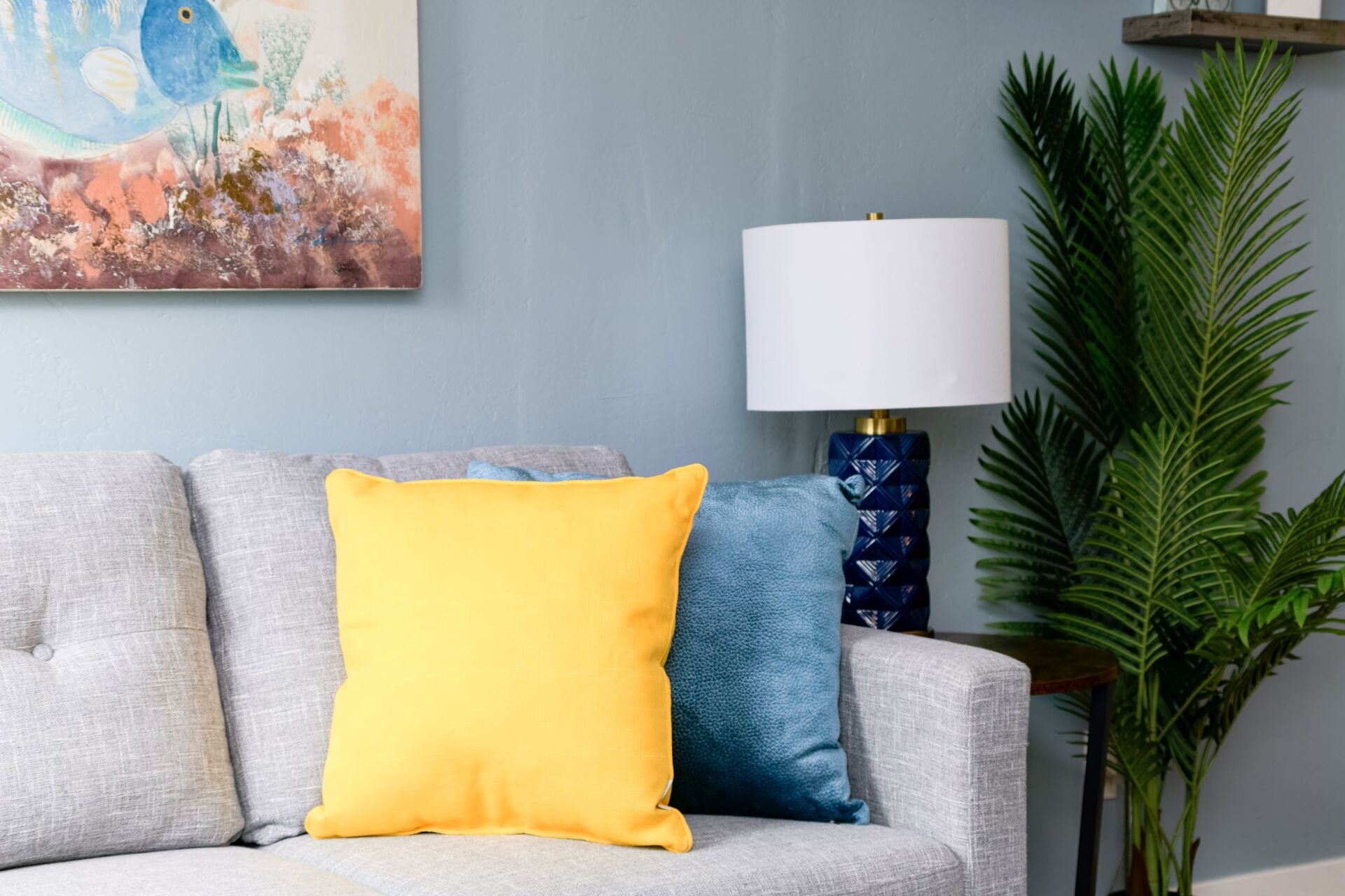 A living room with a couch , lamp , and painting on the wall.