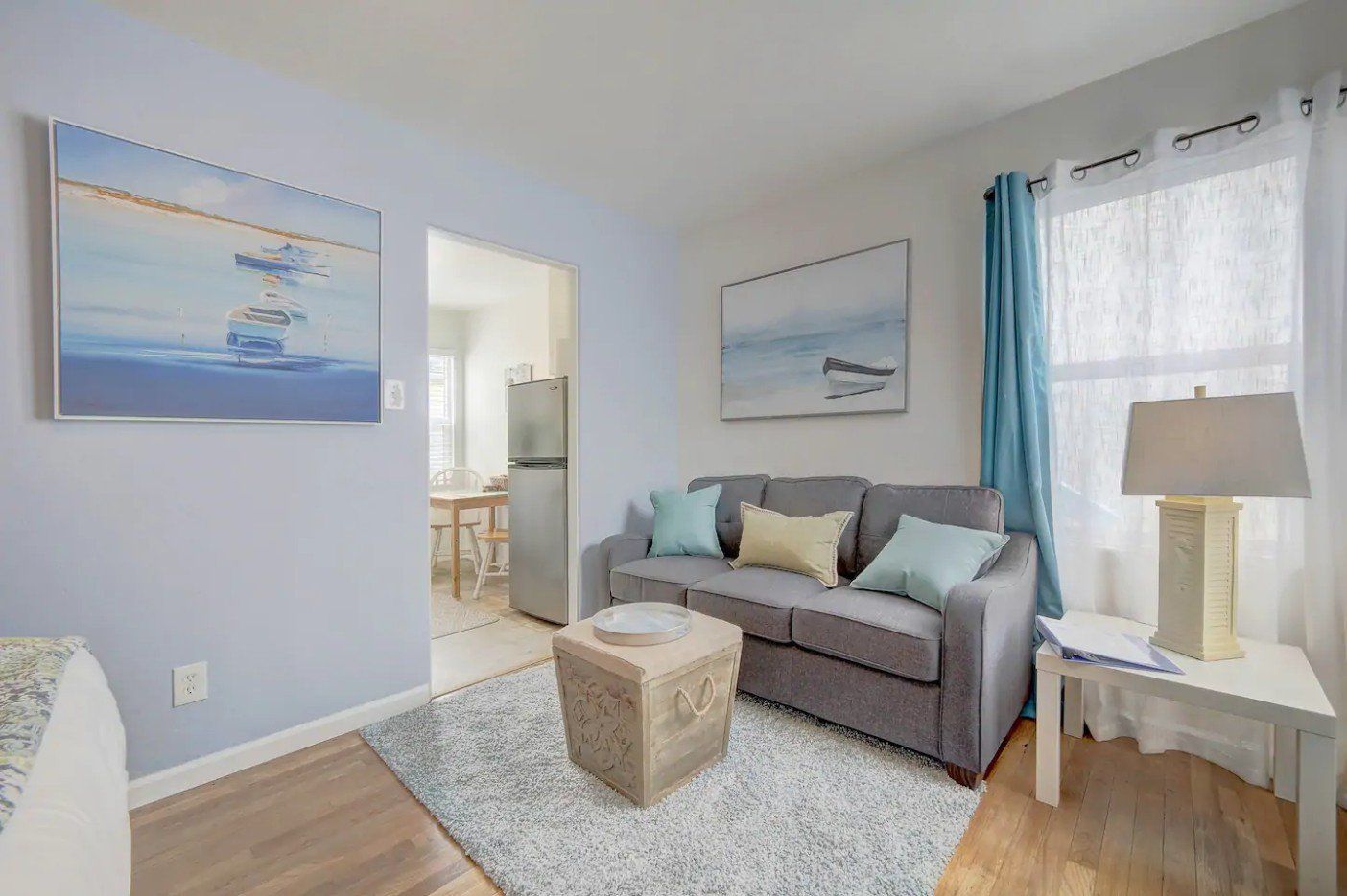 a living room with a couch , table , lamp and paintings on the wall .