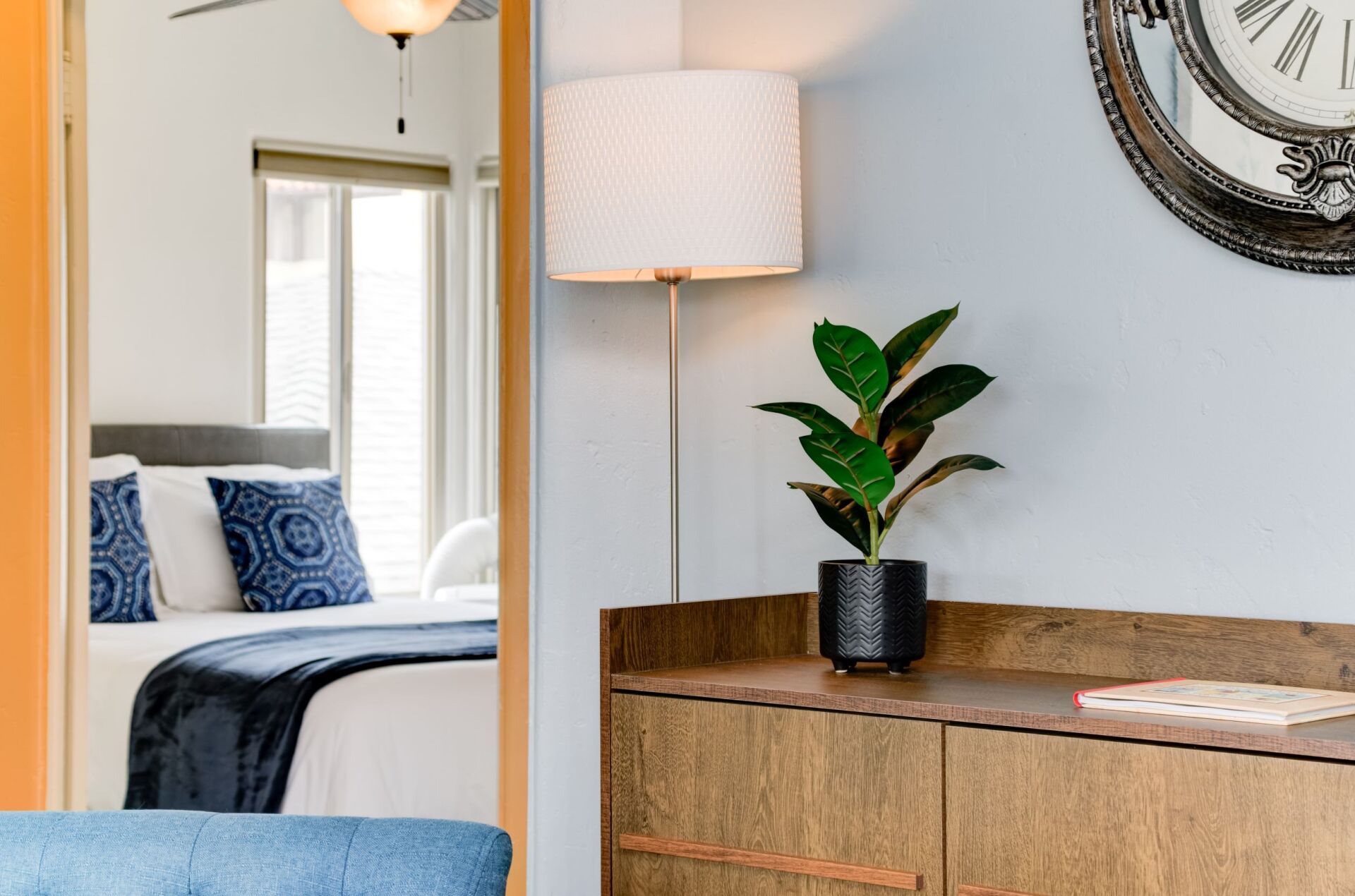 A bedroom with a bed , dresser , lamp and clock on the wall.