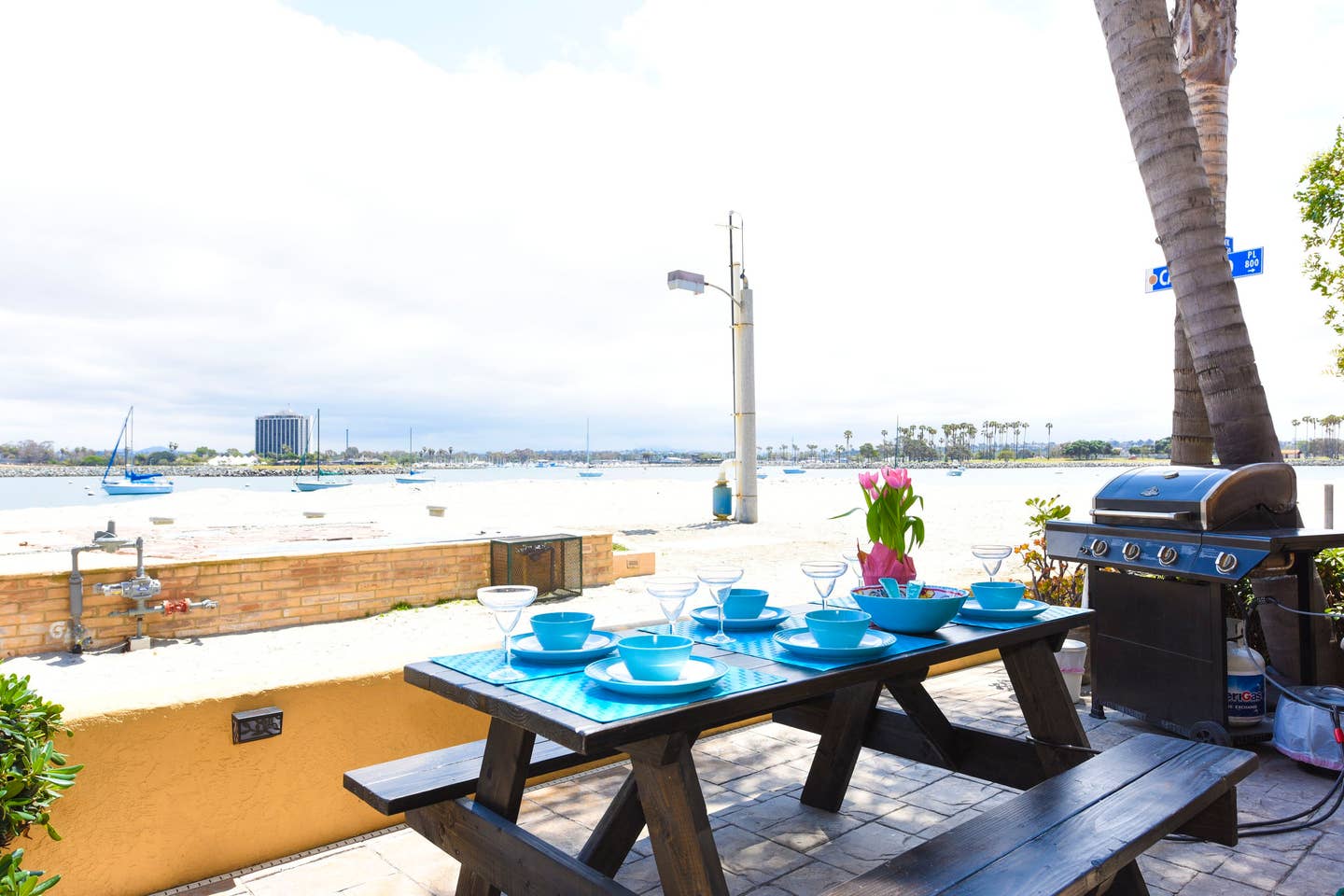 A picnic table with plates and bowls on it is sitting on a patio overlooking a body of water.