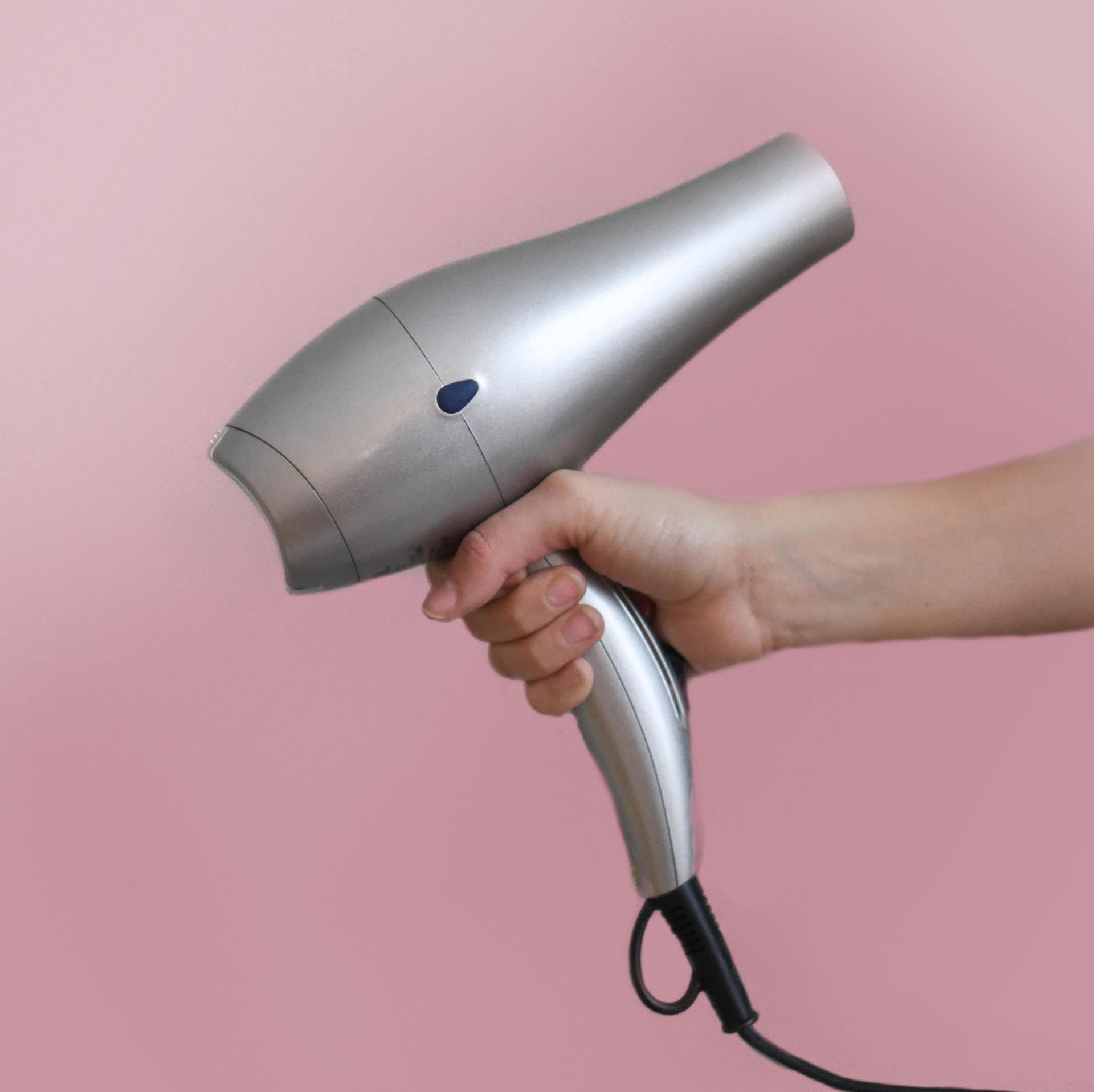 a person is holding a hair dryer in their hand against a pink background .