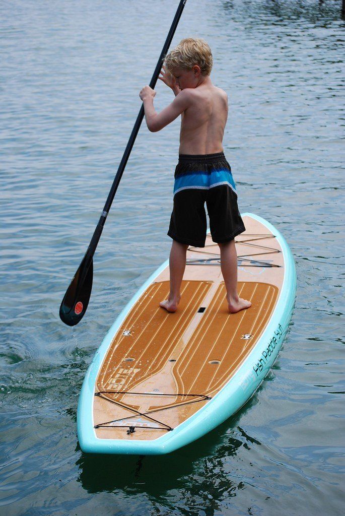 a young boy is standing on a paddle board in the water