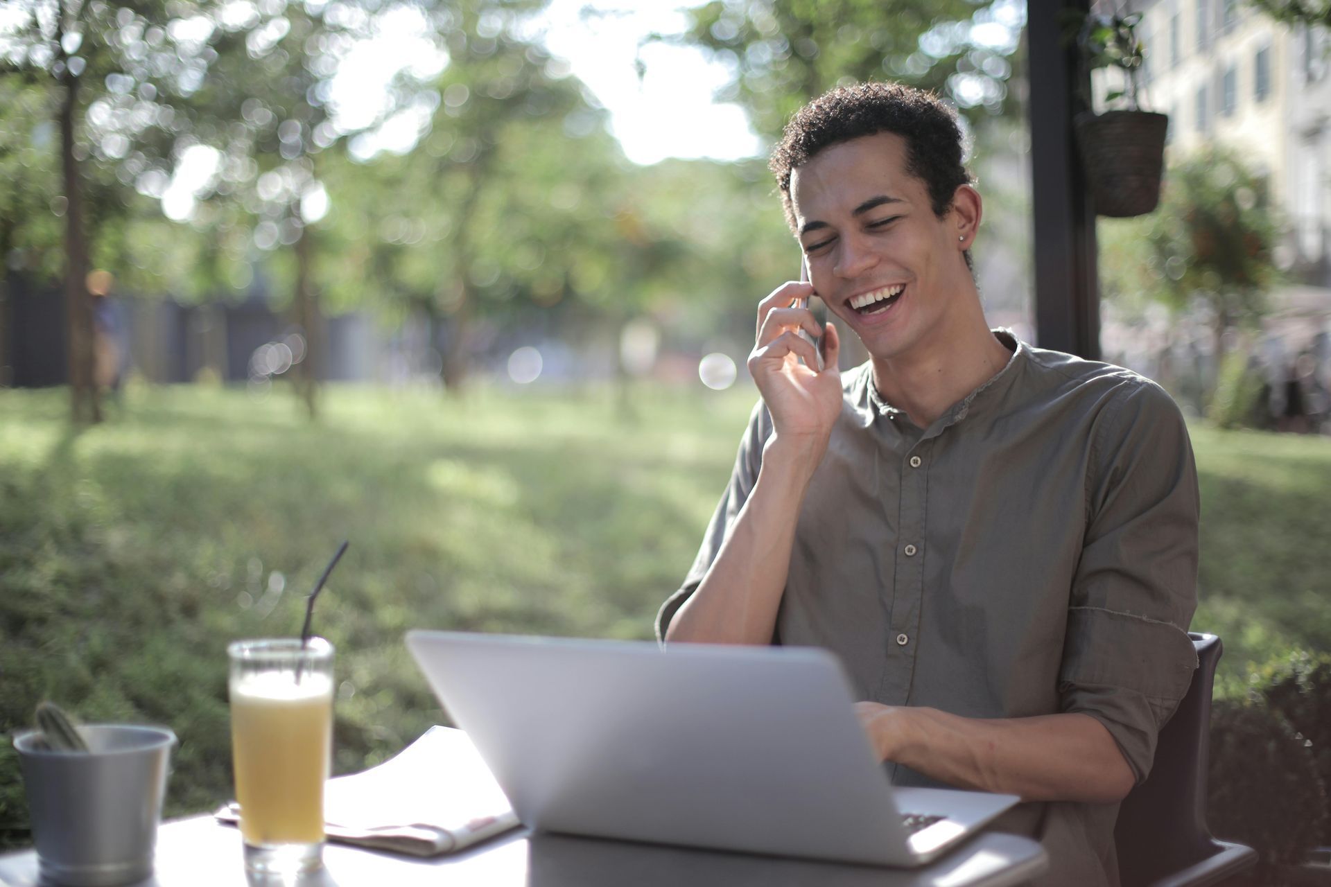 A man is sitting at a table with a laptop and talking on a cell phone.