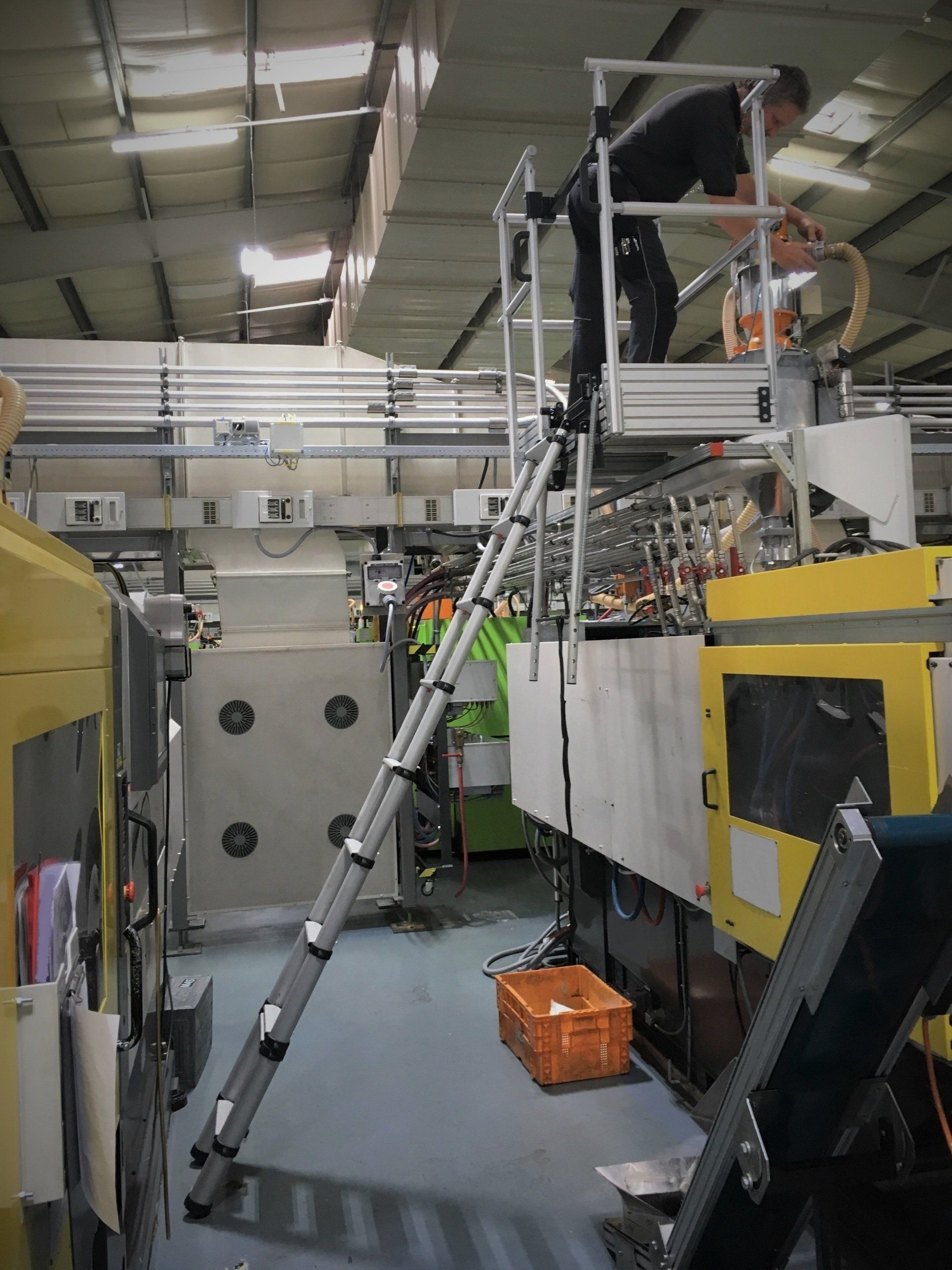 Ein Mann steht in einer Fabrik auf einer Leiter und arbeitet an einer Maschine.