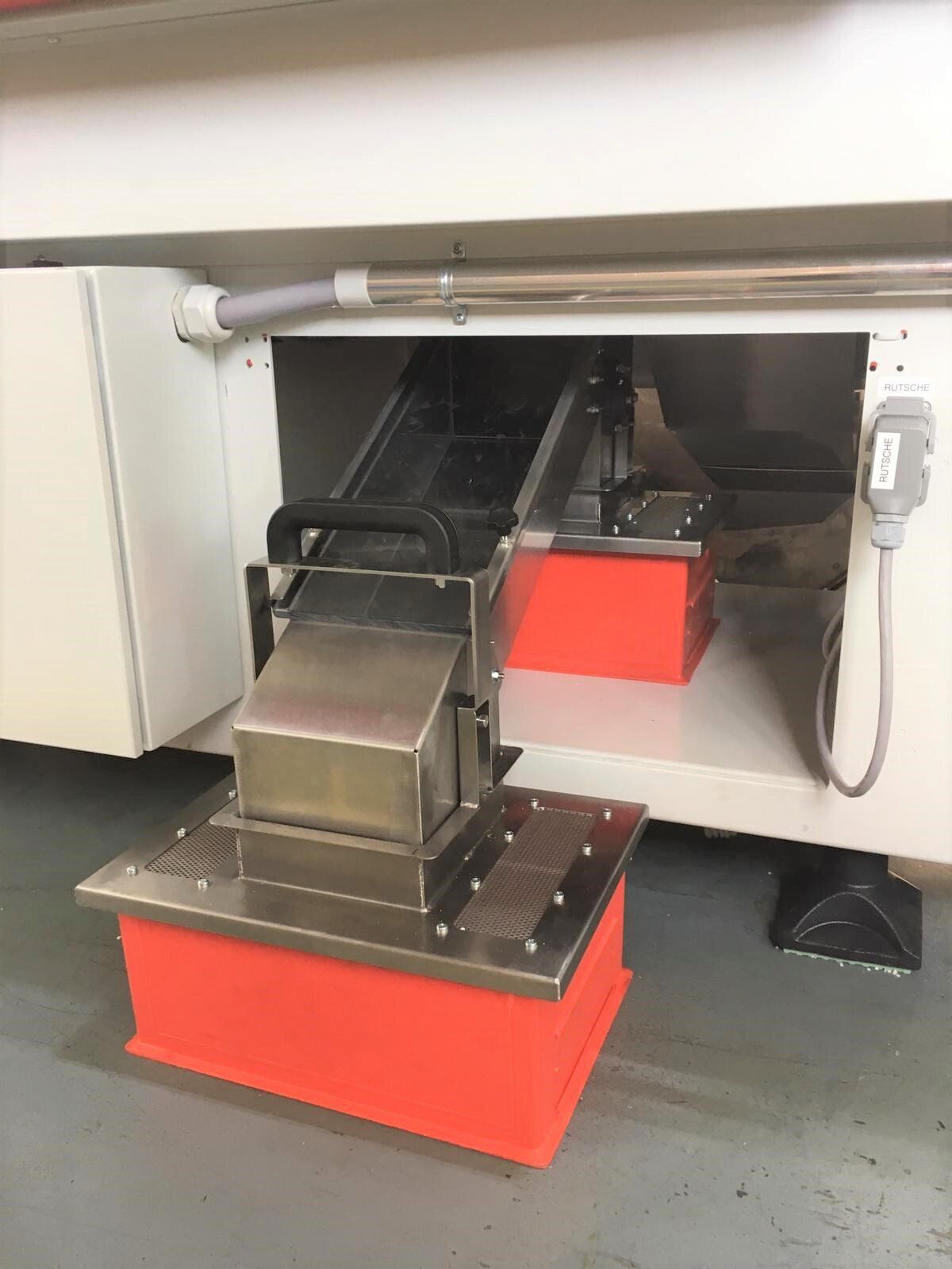 Eine Maschine steht mit geöffneter Tür auf einem Betonboden.