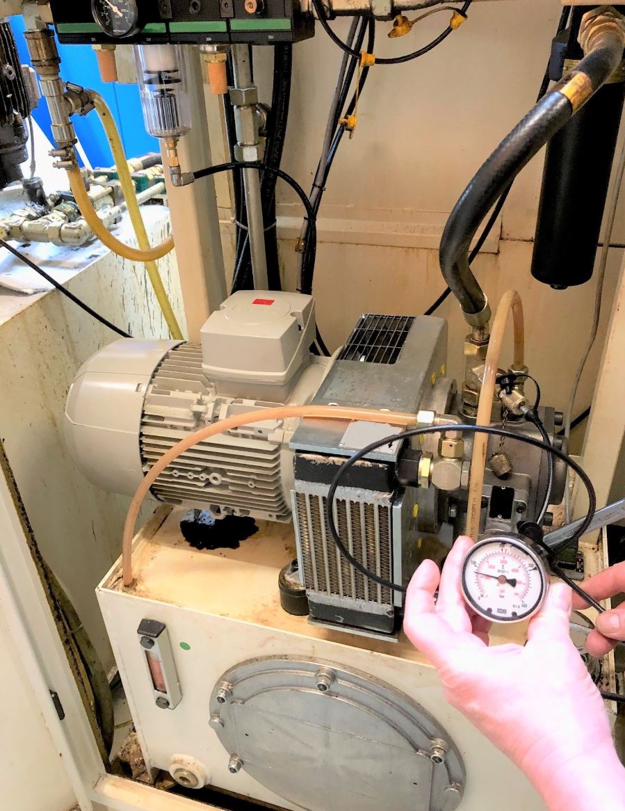 Eine Person hält ein Druckmessgerät vor eine Maschine.