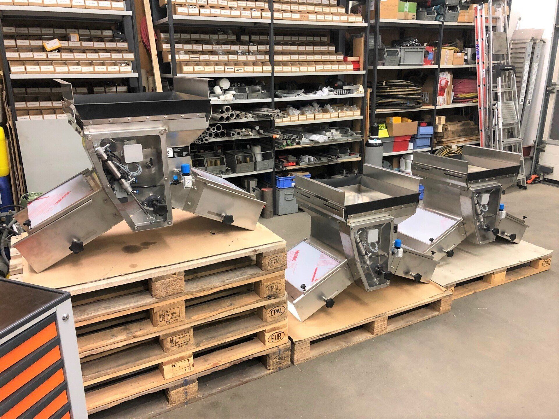 Eine Gruppe von Maschinen aus Edelstahl steht auf Holzpaletten in einem Lagerhaus.