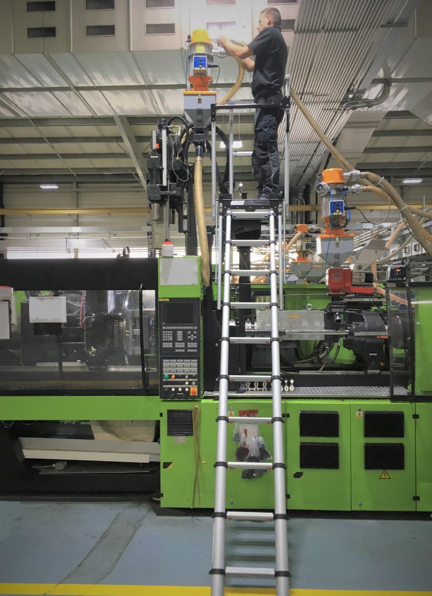 Ein Mann auf einer Leiter, der an einer Maschine in einer Fabrik arbeitet