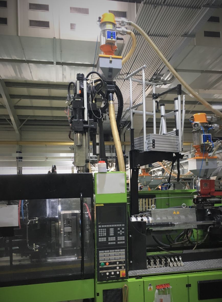 In einer Fabrik steht eine grüne Maschine, an die ein Schlauch angeschlossen ist.