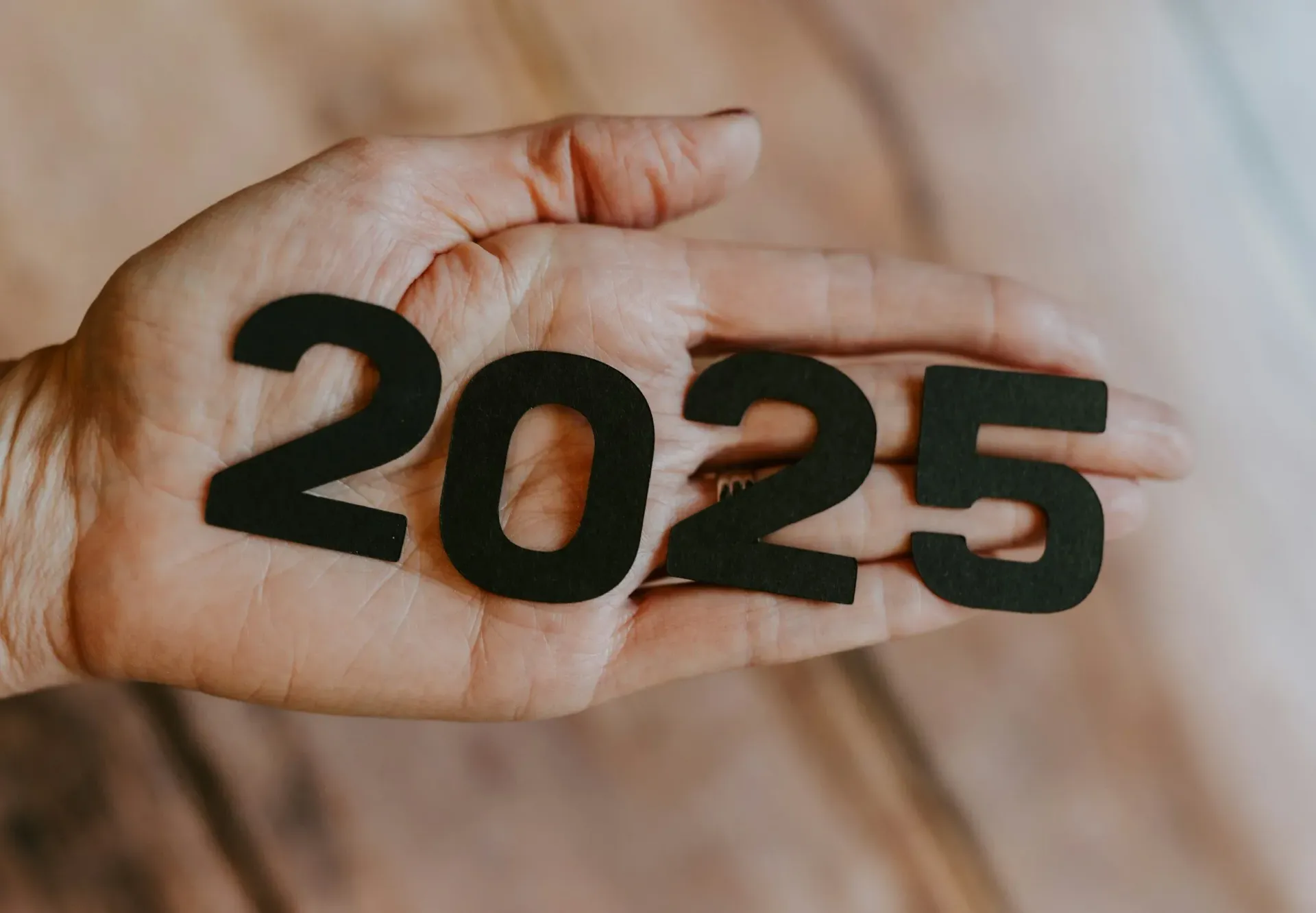 Hand holding black “2025” cutout numbers on a light background
