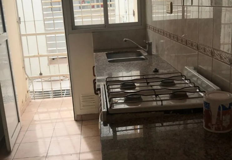 Pequeña cocina con estufa de gas, fregadero, piso de baldosas y una puerta que da a una luminosa zona exterior.