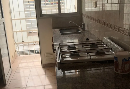 Pequeña cocina con estufa de gas, fregadero, piso de baldosas y una puerta que da a una luminosa zona exterior.