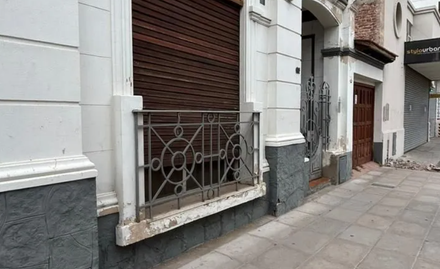 Acera junto a un edificio blanco con una contraventana marrón cerrada y una barandilla metálica