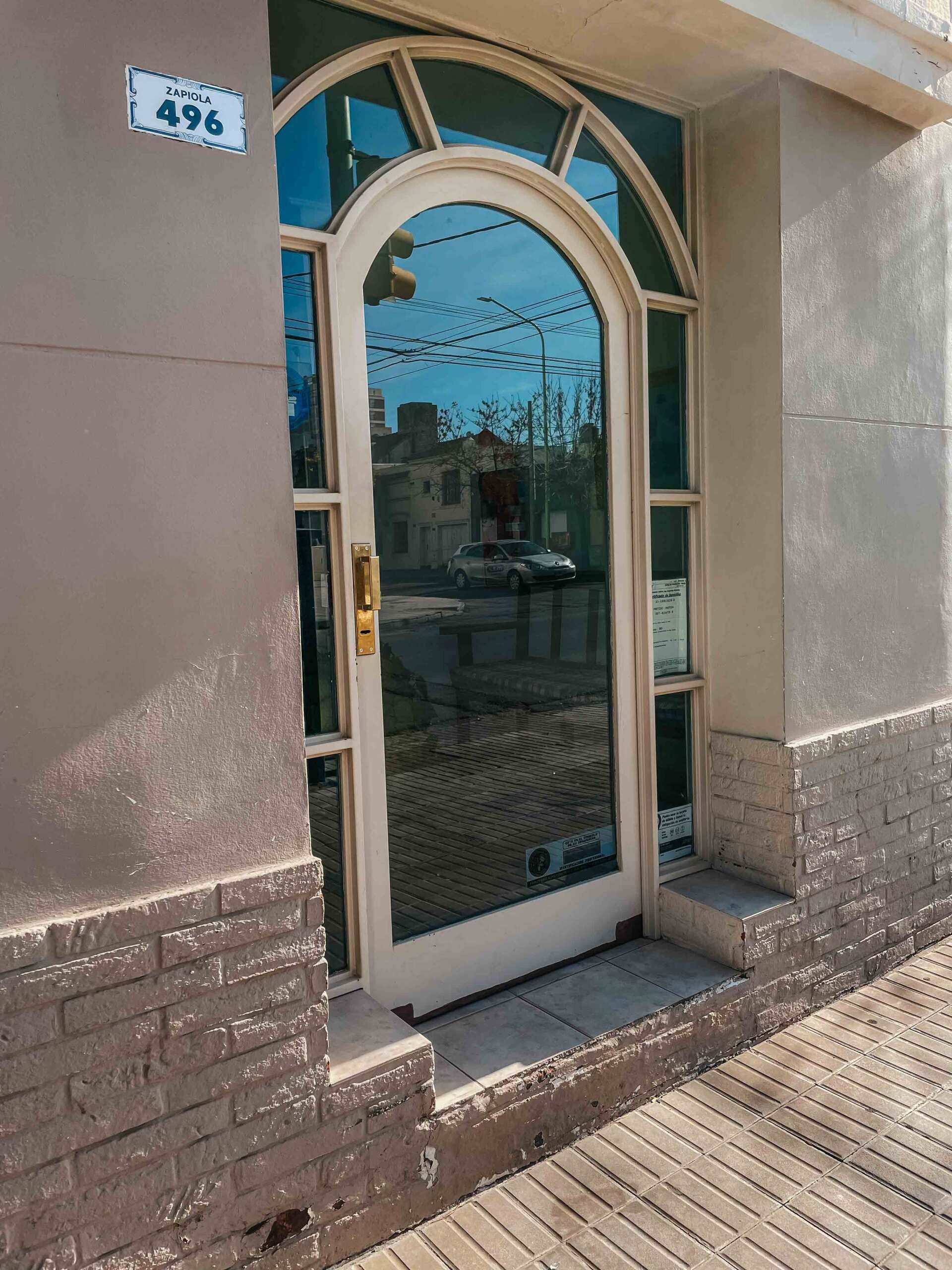 Exterior de un edificio de color beige con una puerta de cristal con marco blanco.