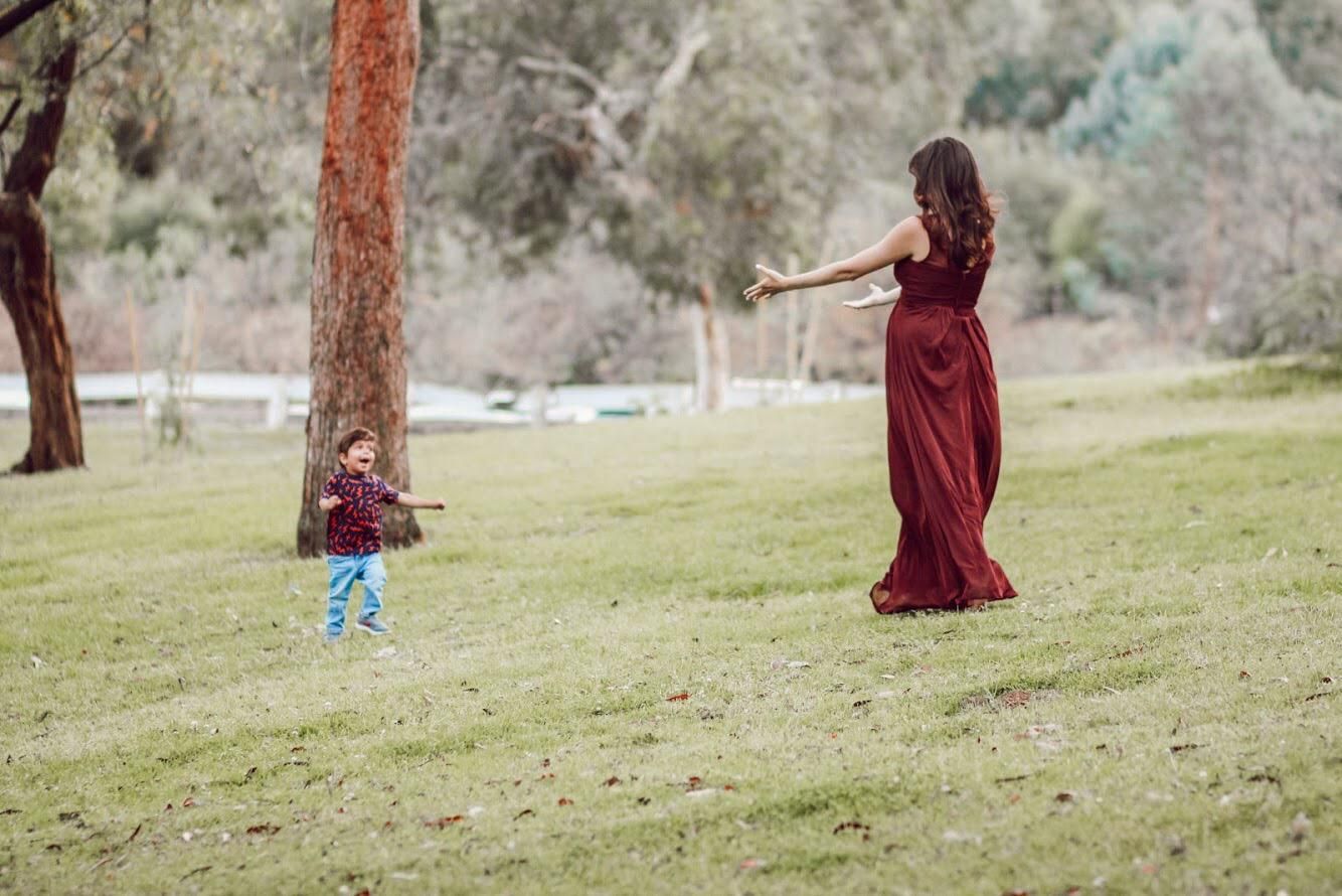 A pregnant woman in a red dress is playing with a little boy in a park.