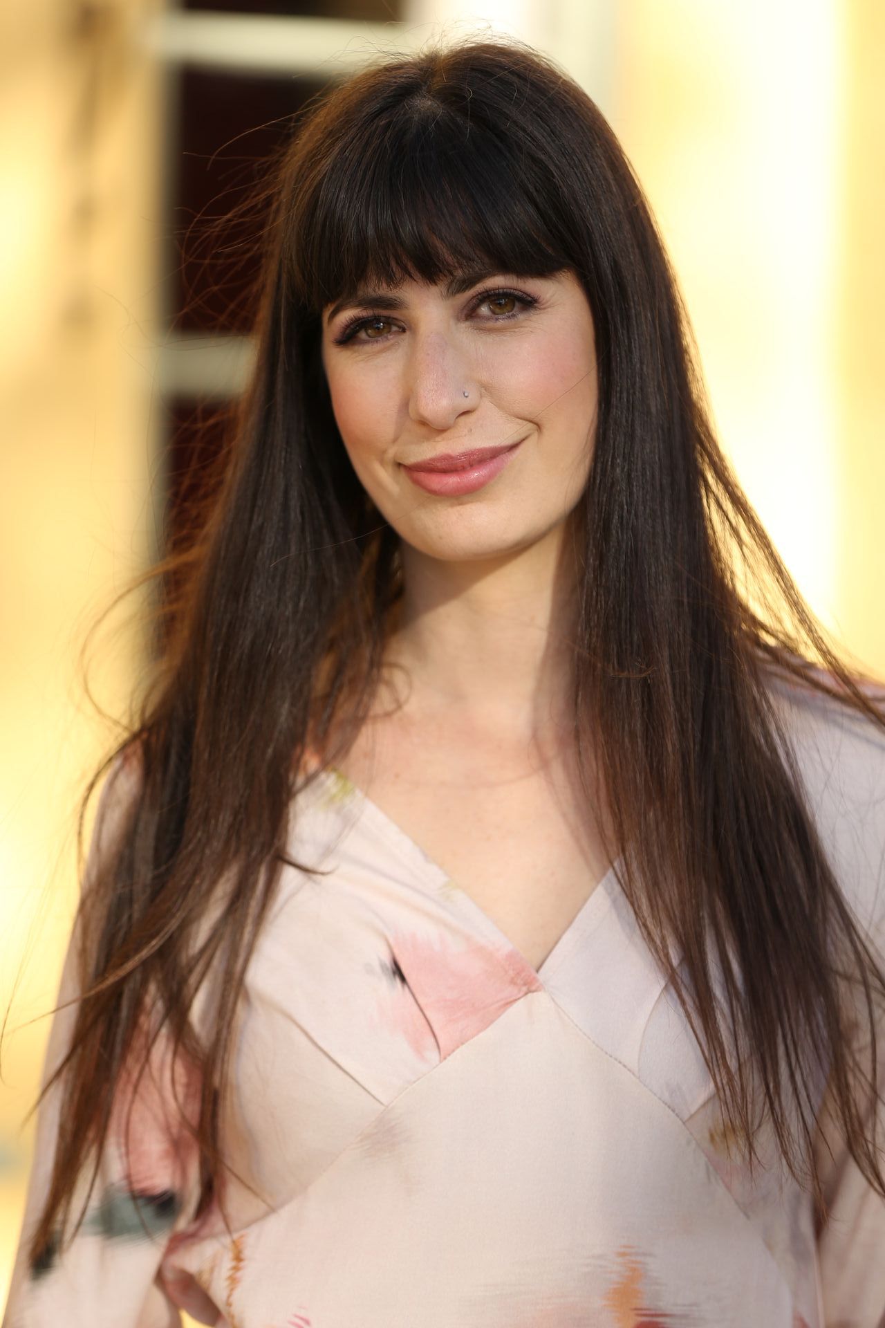 A woman with long hair and a nose ring is smiling for the camera.
